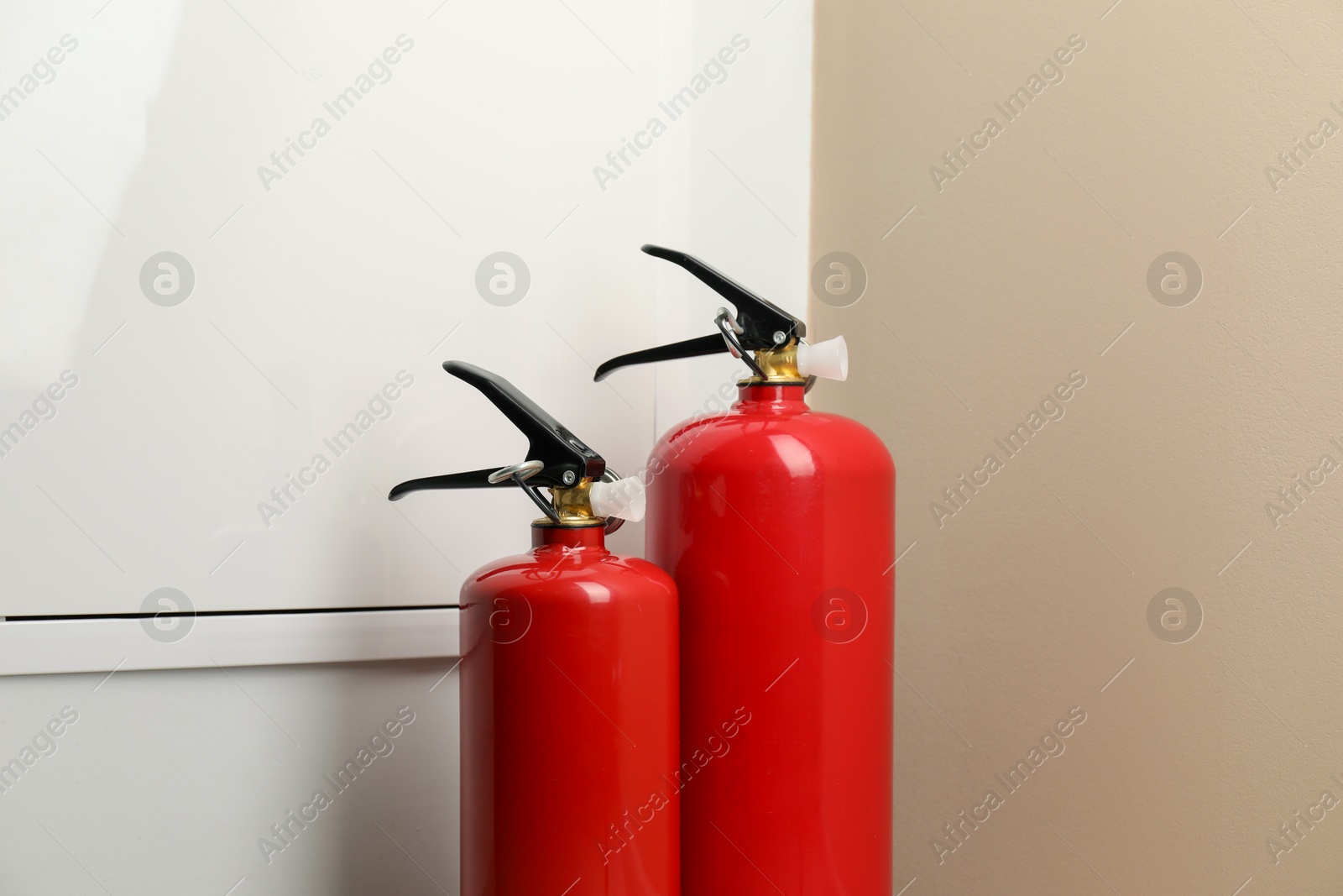 Photo of Two fire extinguishers near beige wall indoors