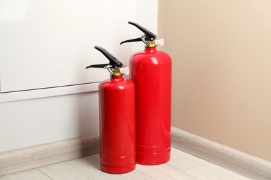 Photo of Fire extinguishers on floor near beige wall indoors