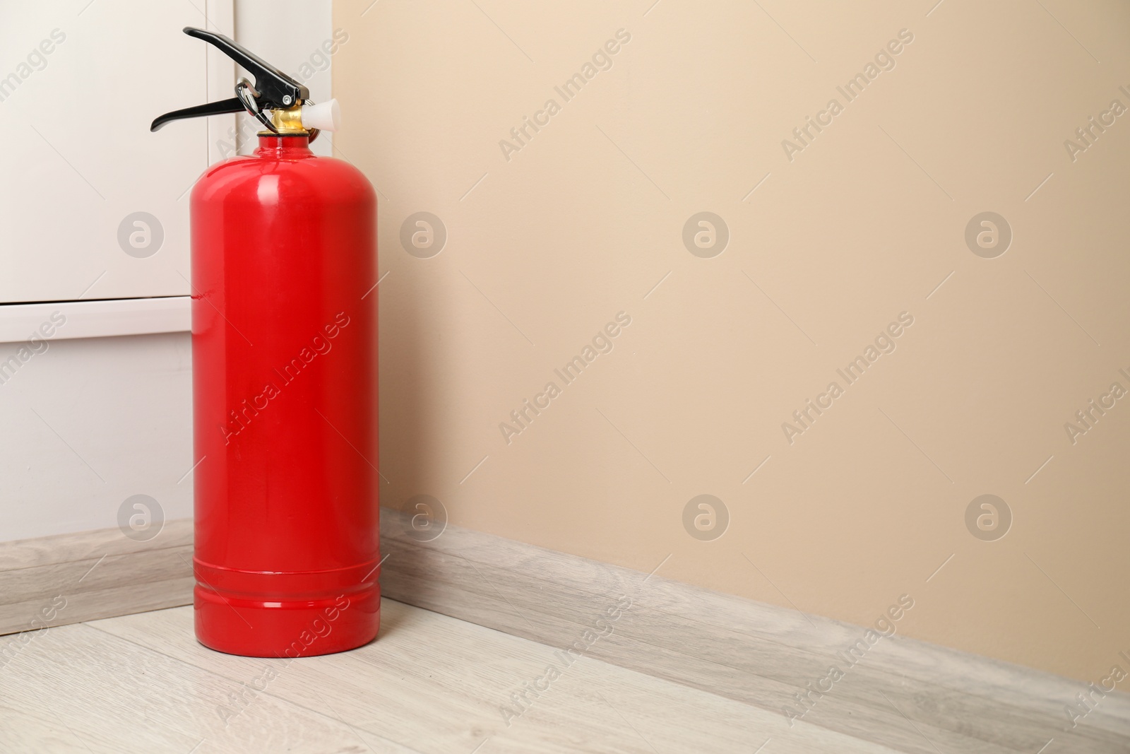 Photo of Fire extinguisher on floor near beige wall indoors, space for text