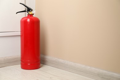 Photo of Fire extinguisher on floor near beige wall indoors, space for text