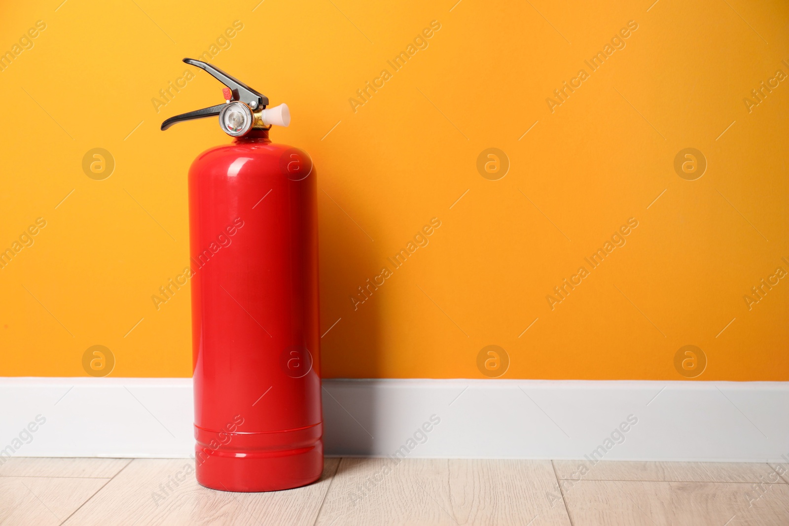 Photo of Fire extinguisher on floor near orange wall, space for text