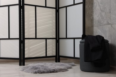 Stylish folding screen and pouf near grey wall indoors. Interior element