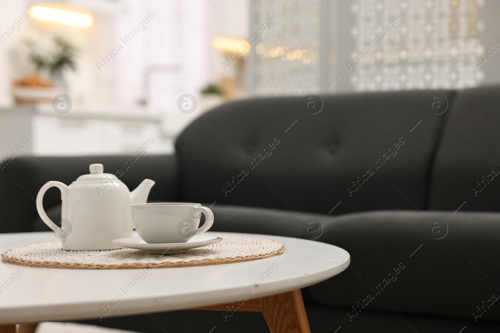 Photo of Teapot with cup on table, sofa and folding screen indoors, space for text