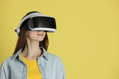 Woman using virtual reality headset on yellow background, space for text