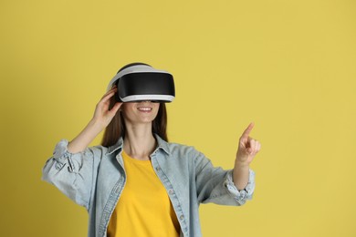 Smiling woman using virtual reality headset on yellow background, space for text