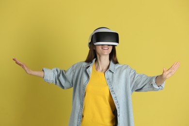 Photo of Smiling woman using virtual reality headset on yellow background