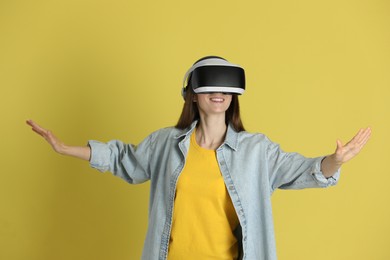 Smiling woman using virtual reality headset on yellow background