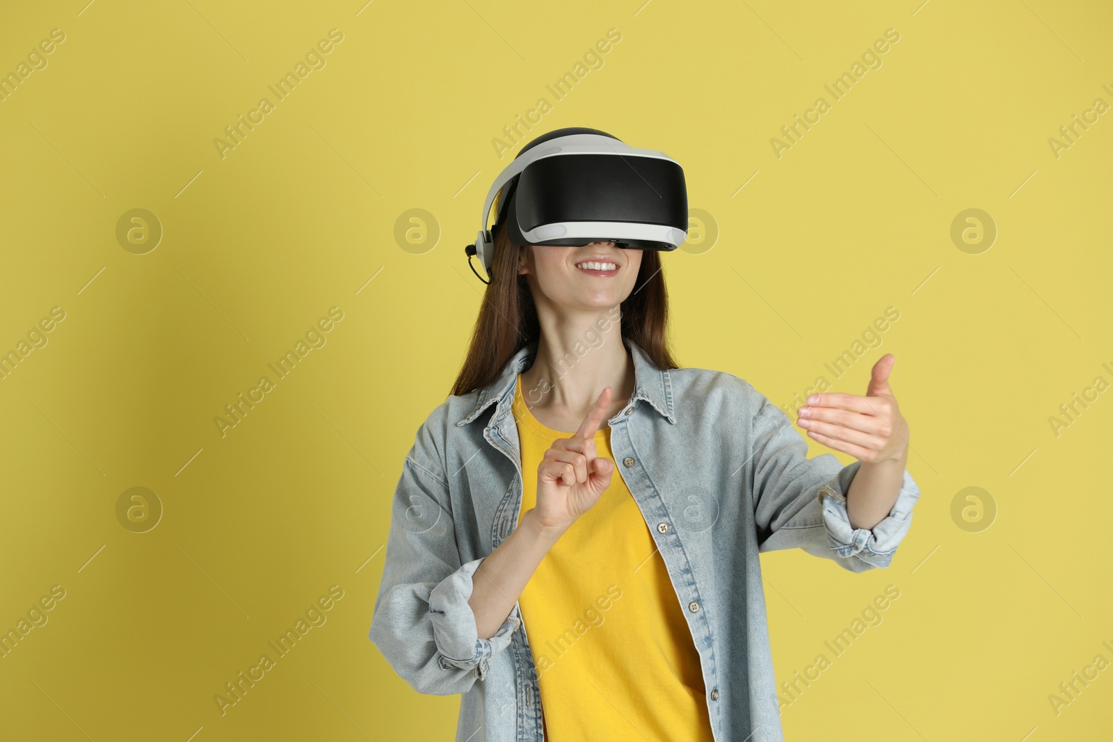 Photo of Smiling woman using virtual reality headset on yellow background