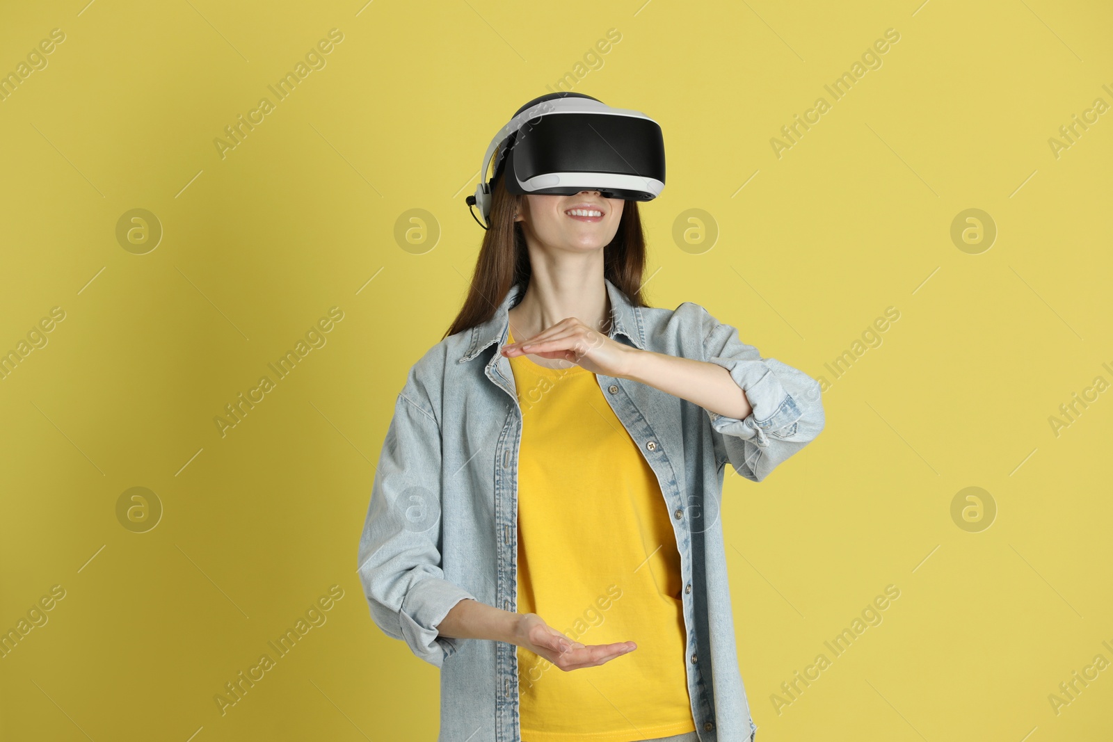 Photo of Smiling woman using virtual reality headset on yellow background