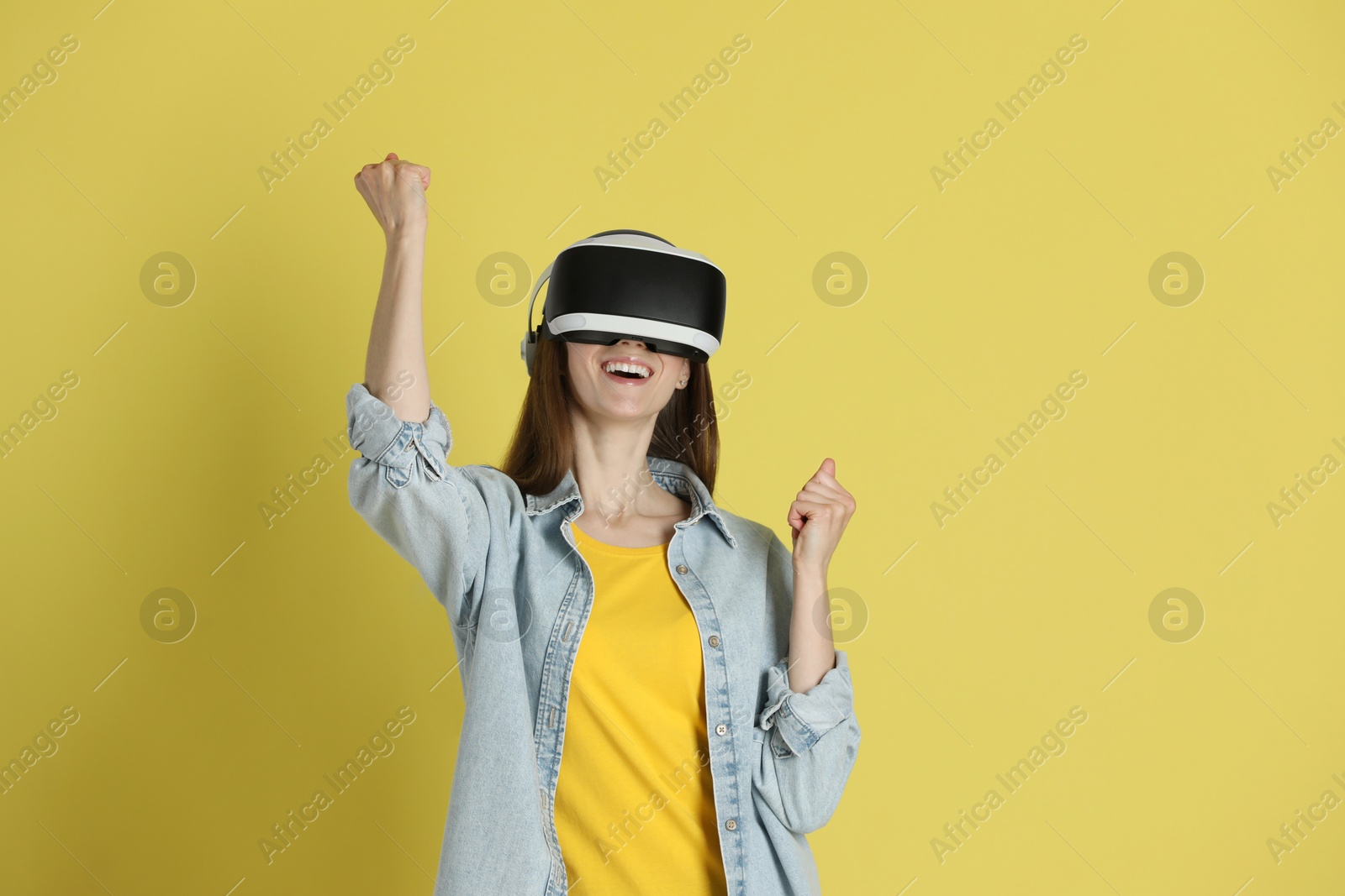 Photo of Smiling woman using virtual reality headset on yellow background