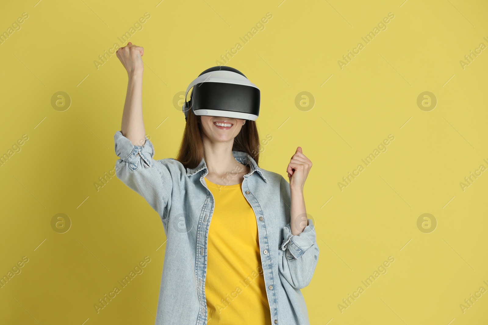 Photo of Smiling woman using virtual reality headset on yellow background