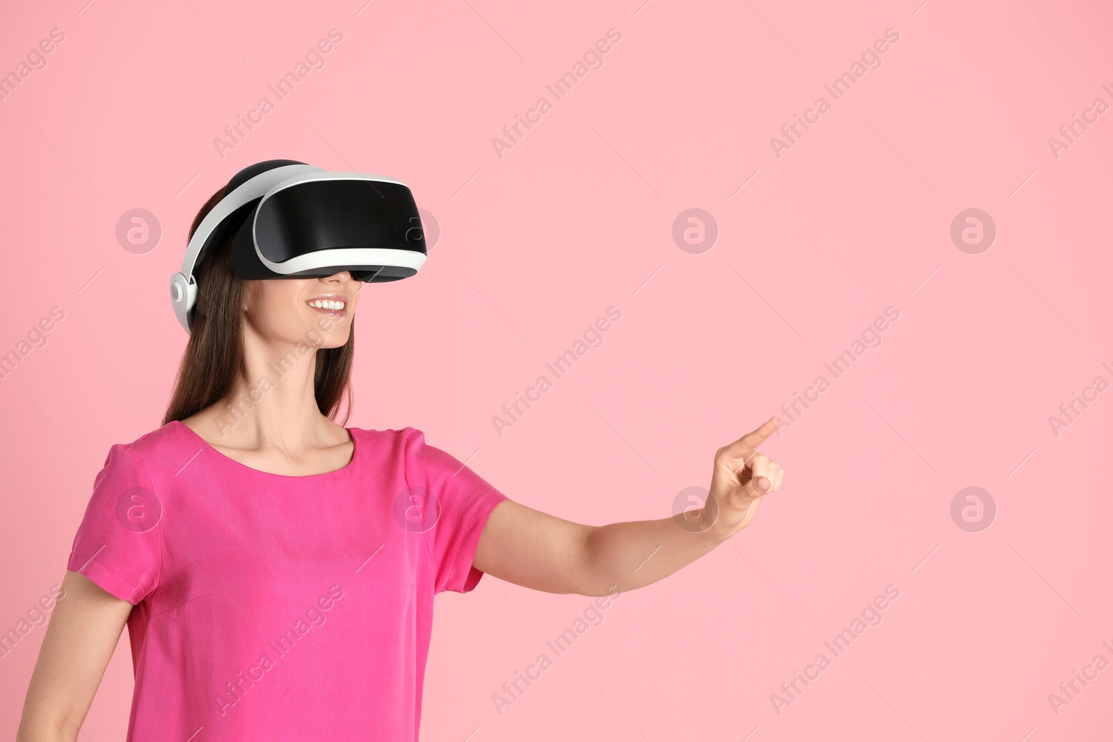 Photo of Smiling woman using virtual reality headset on pink background, space for text