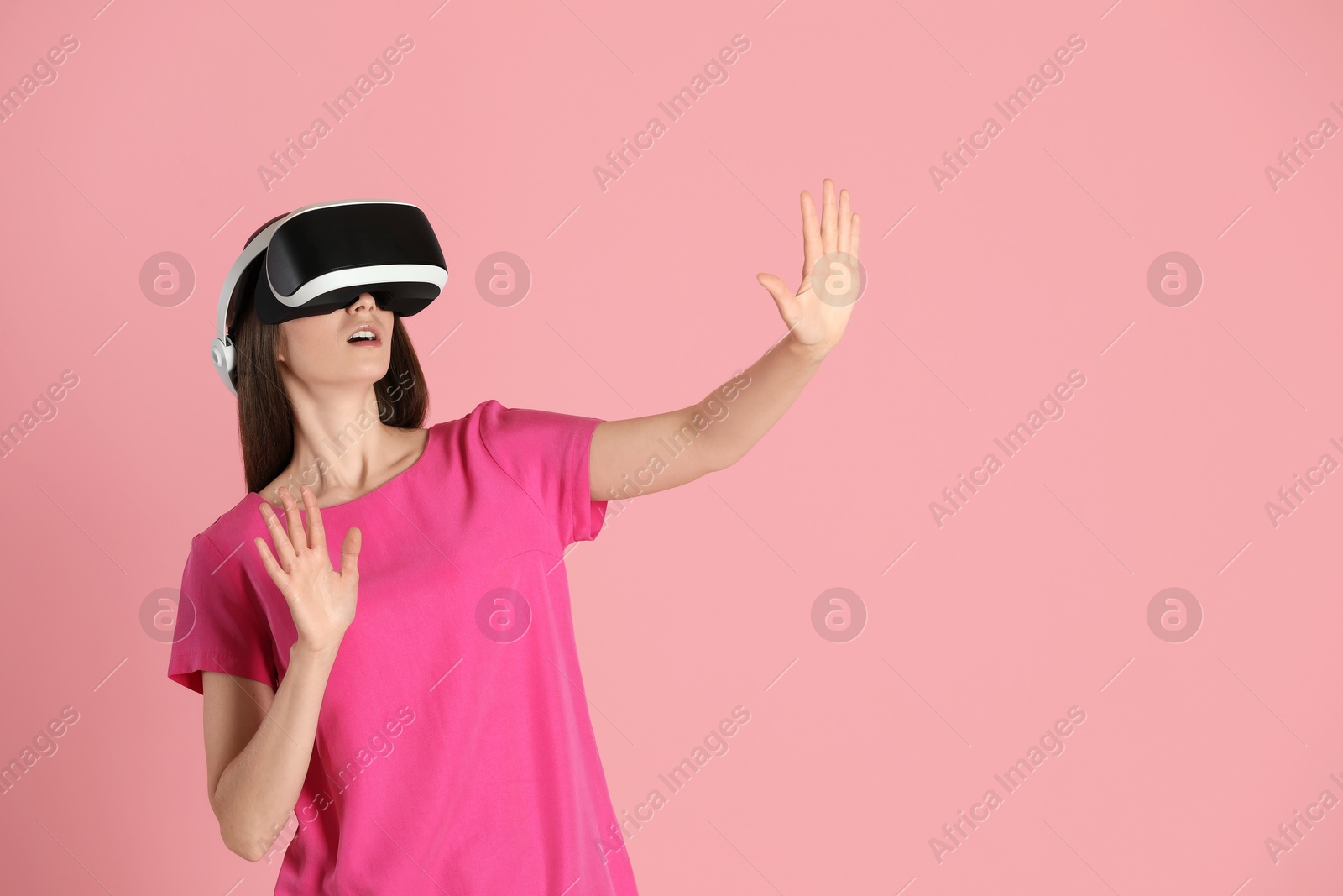 Photo of Surprised woman using virtual reality headset on pink background, space for text