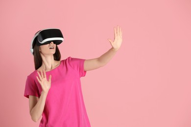 Surprised woman using virtual reality headset on pink background, space for text