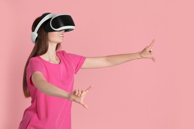 Smiling woman using virtual reality headset on pink background