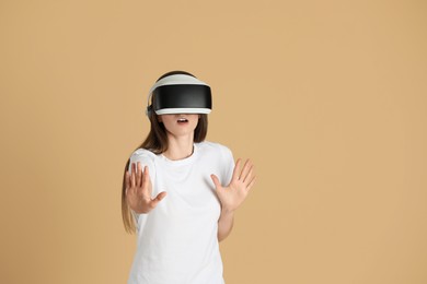 Surprised woman using virtual reality headset on beige background, space for text