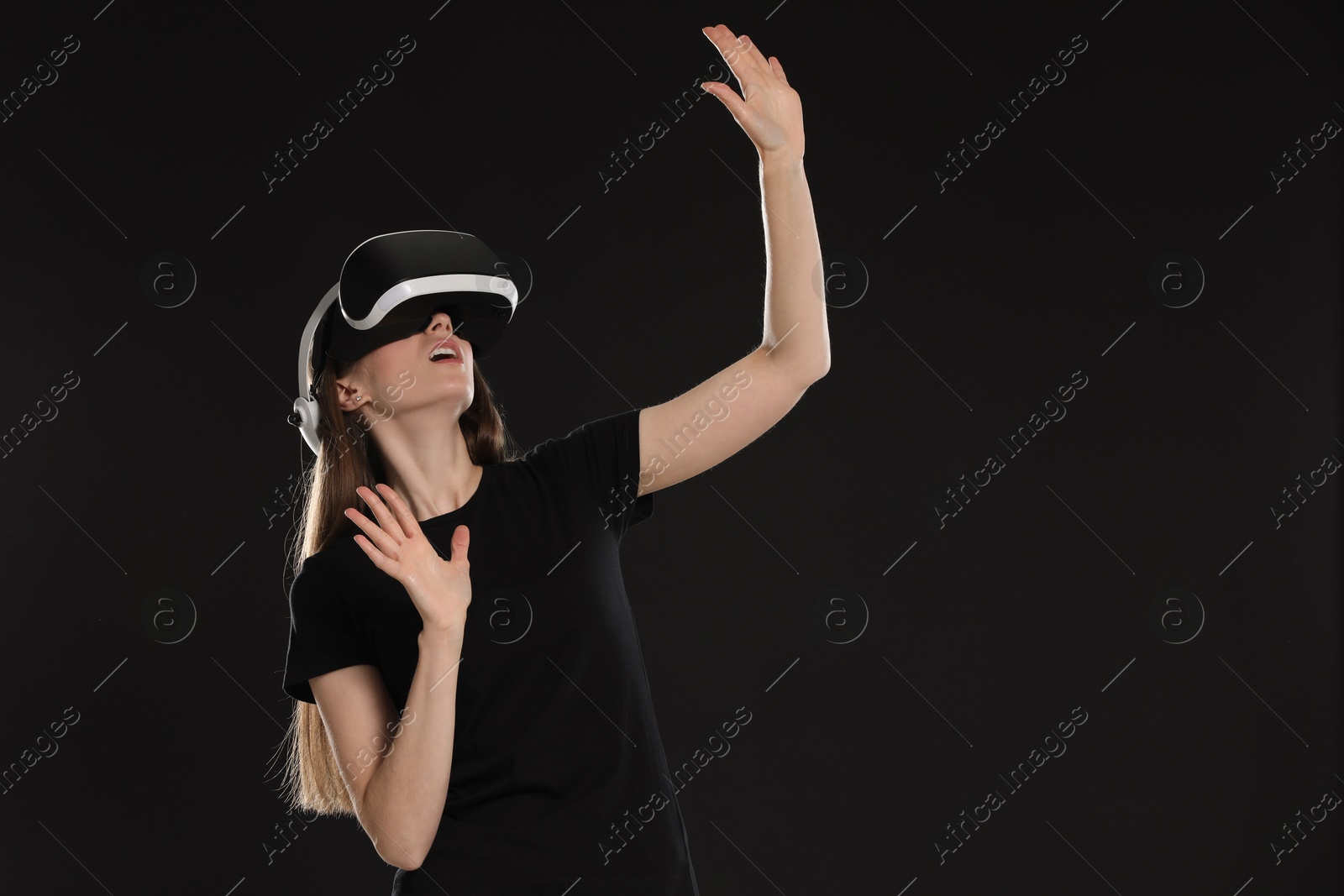 Photo of Surprised woman using virtual reality headset on black background, space for text