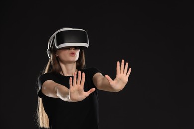 Surprised woman using virtual reality headset on black background, space for text