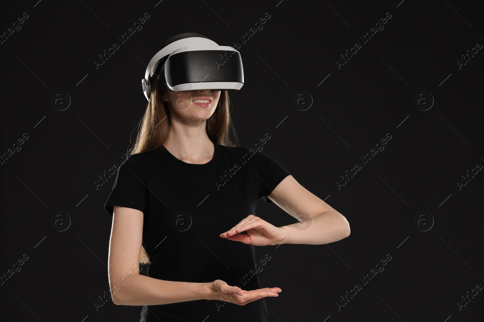 Photo of Smiling woman using virtual reality headset on black background, space for text