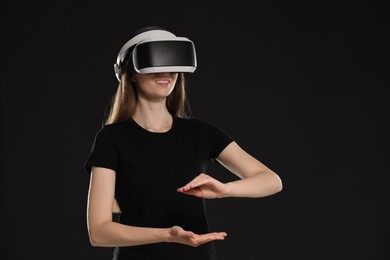 Smiling woman using virtual reality headset on black background, space for text