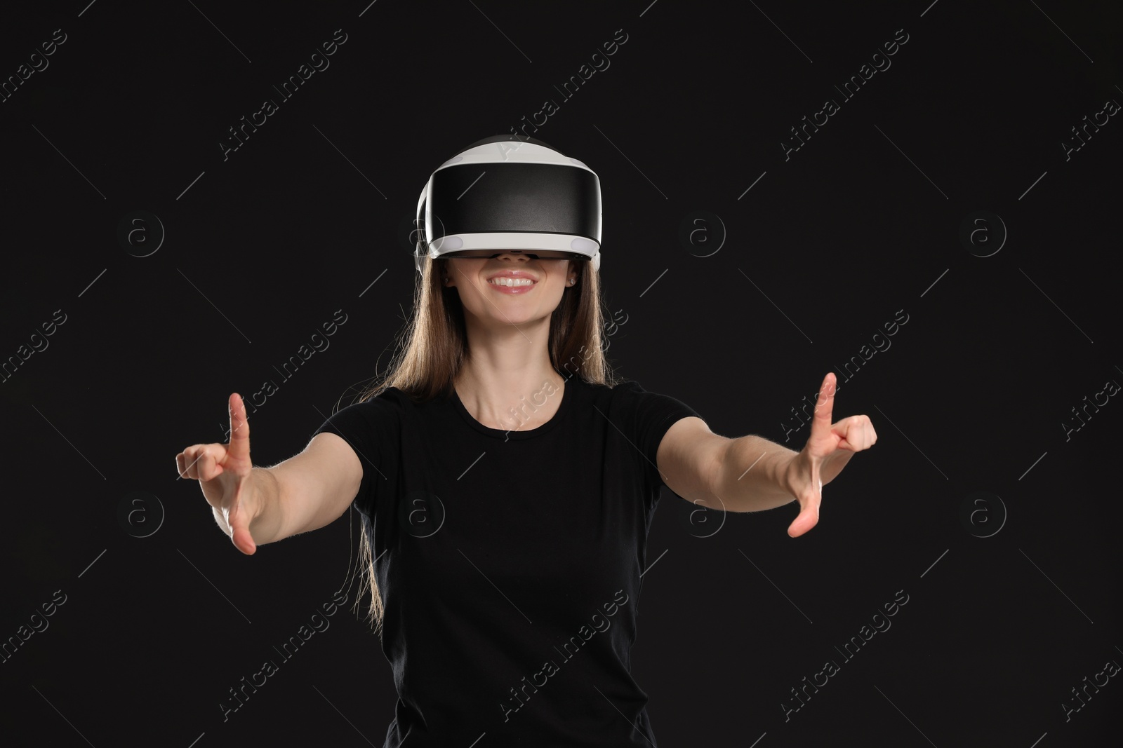 Photo of Smiling woman using virtual reality headset on black background