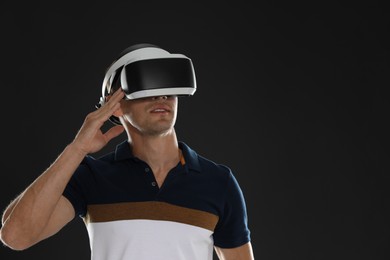 Man using virtual reality headset on black background, space for text