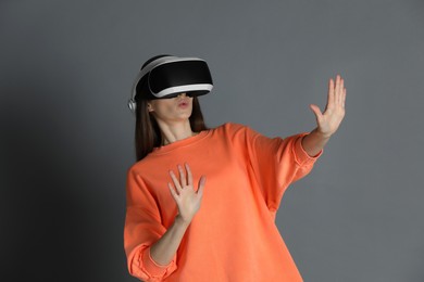 Surprised woman using virtual reality headset on gray background