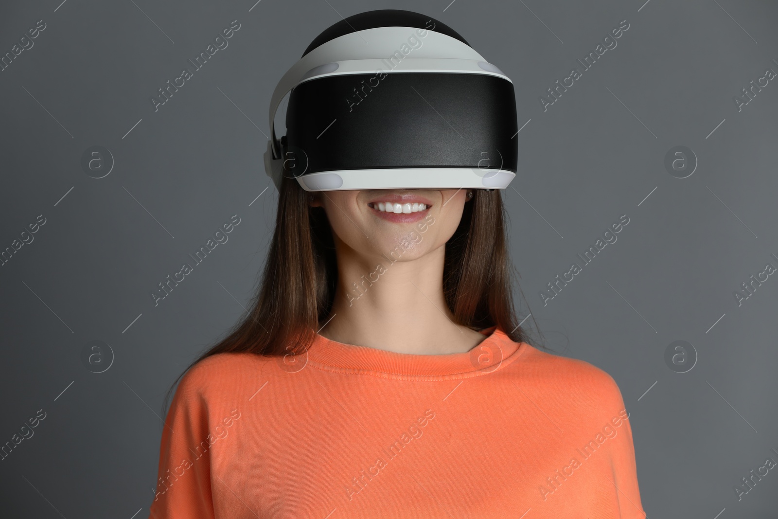 Photo of Smiling woman using virtual reality headset on gray background