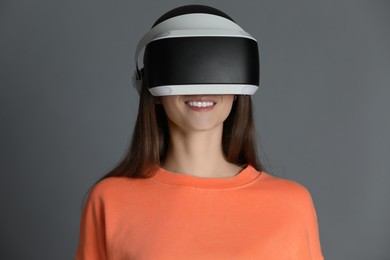 Smiling woman using virtual reality headset on gray background