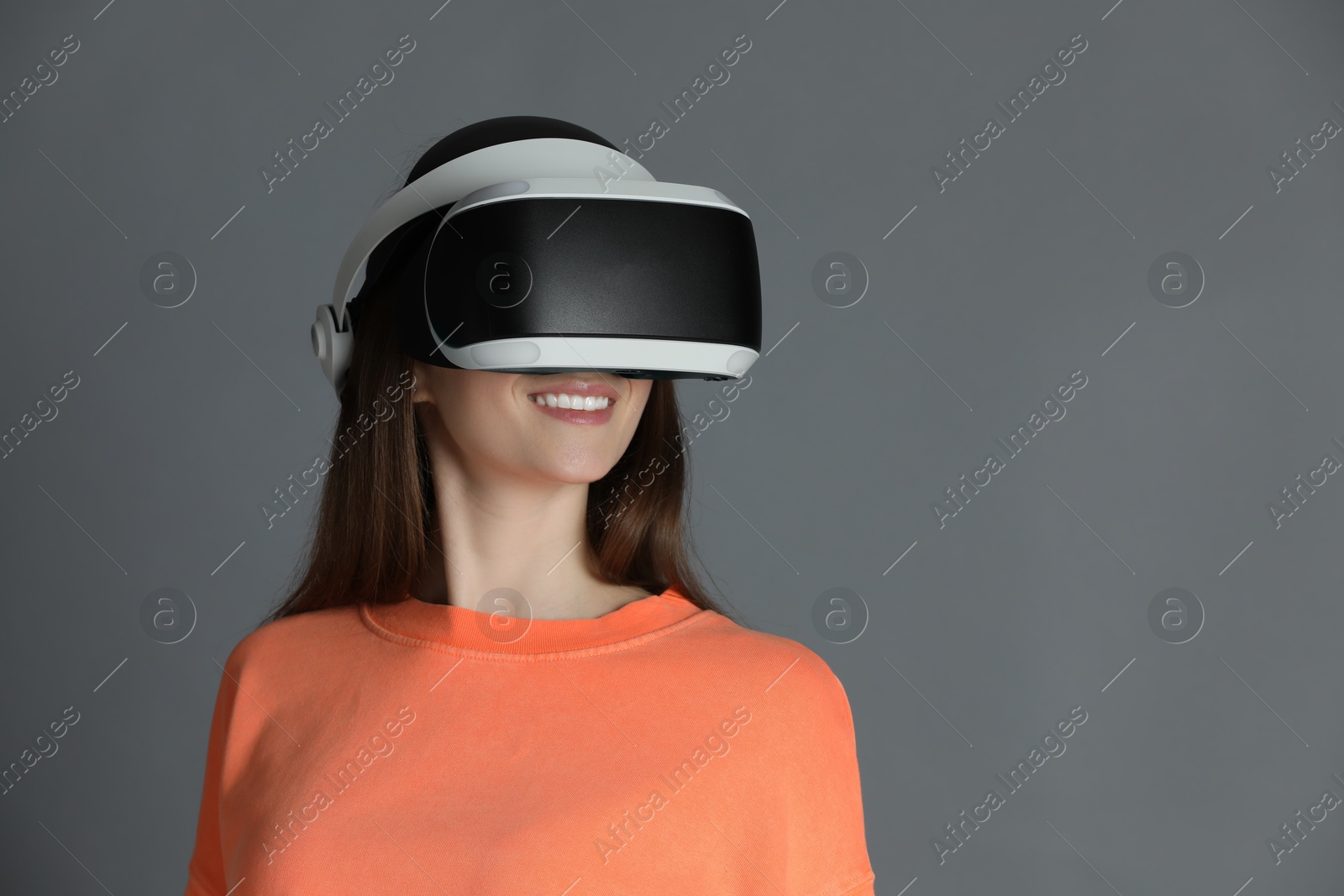 Photo of Smiling woman using virtual reality headset on gray background, space for text
