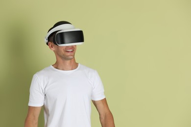 Smiling man using virtual reality headset on light green background, space for text