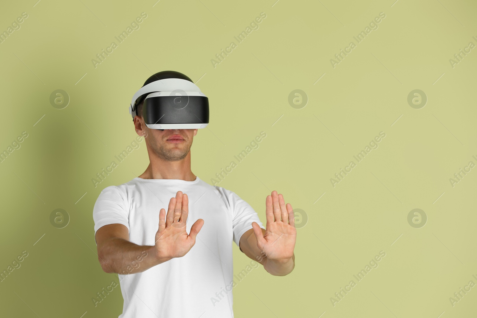 Photo of Surprised man using virtual reality headset on light green background, space for text