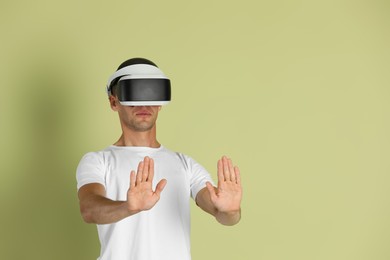 Photo of Surprised man using virtual reality headset on light green background, space for text