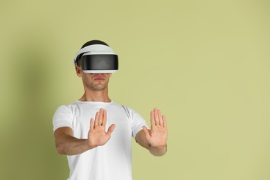 Surprised man using virtual reality headset on light green background, space for text