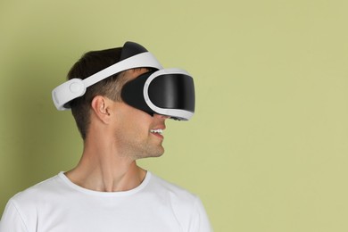 Photo of Smiling man using virtual reality headset on light green background, space for text