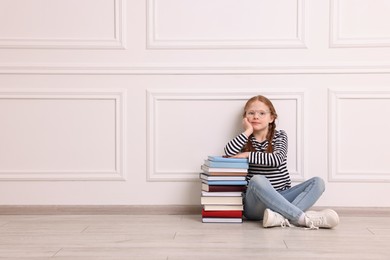 Photo of Cute girl sitting with stack of books indoors. Space for text