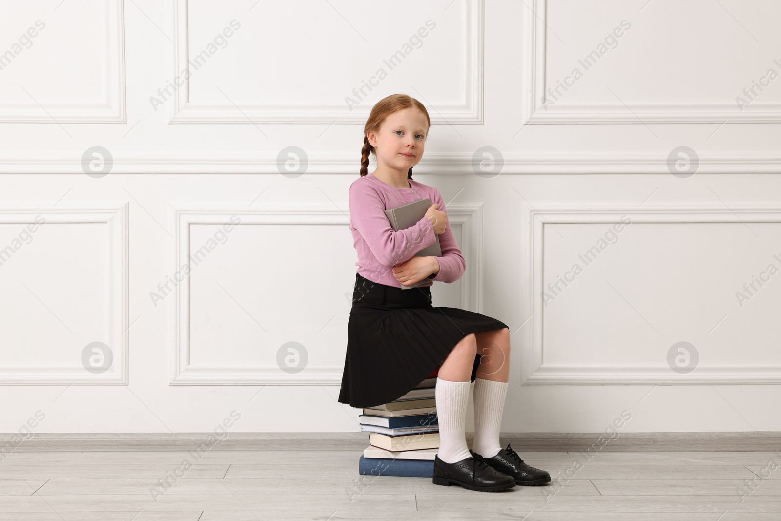 Photo of Little girl sitting on stack of books indoors