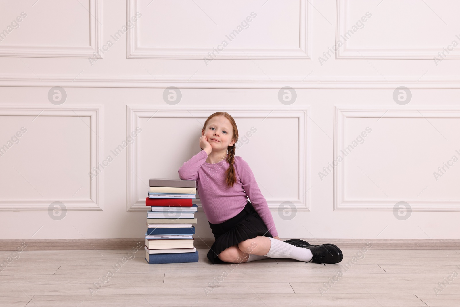 Photo of Little girl with stack of books on floor indoors