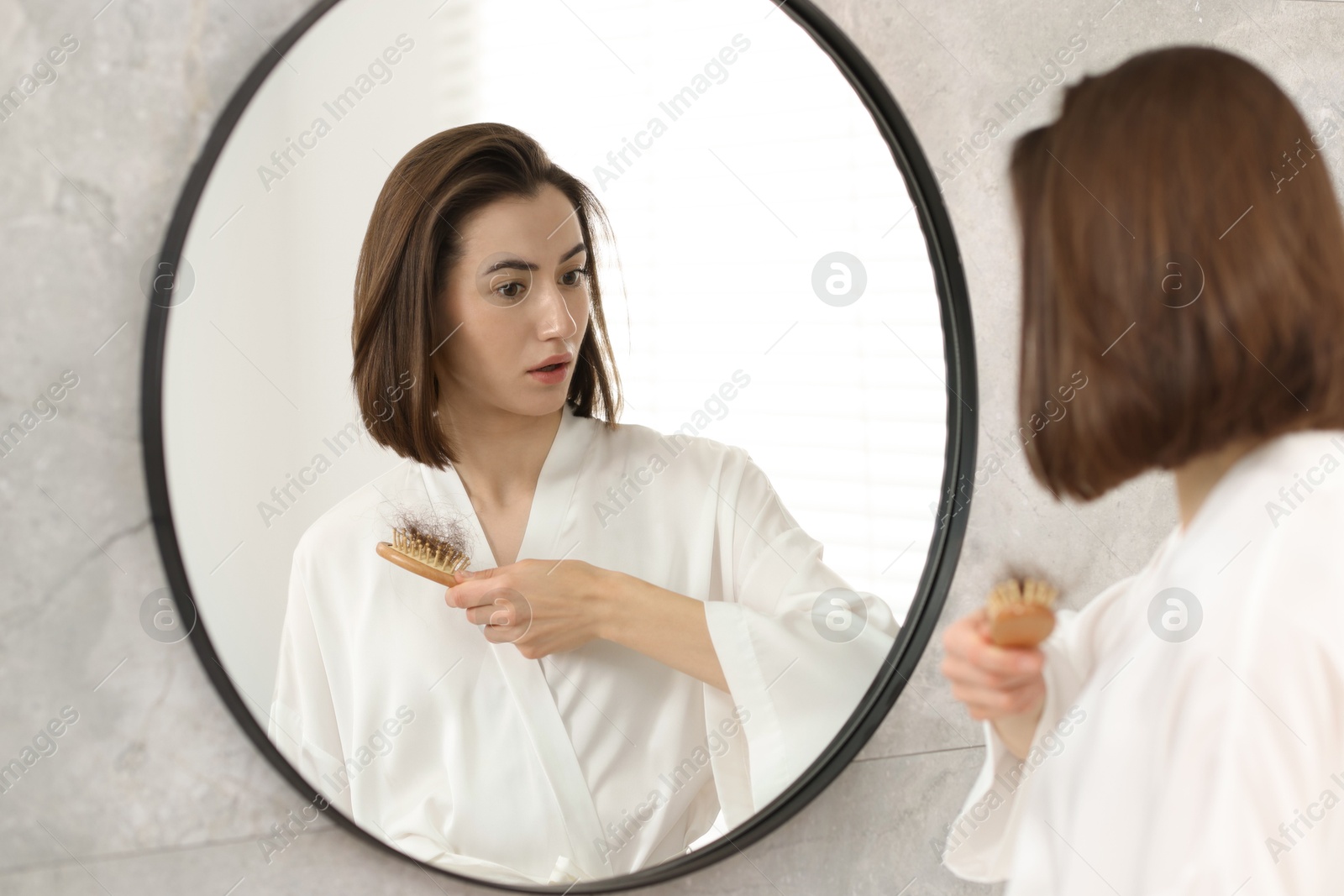 Photo of Young woman with hair loss problem looking at mirror indoors