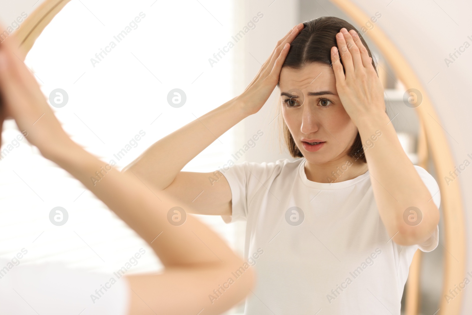 Photo of Sad woman with hair loss problem looking at mirror indoors