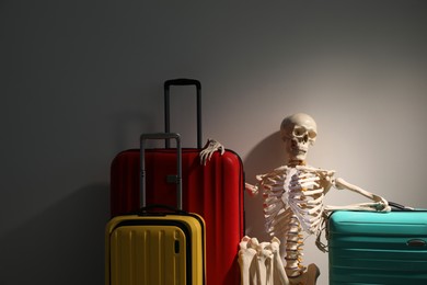 Waiting concept. Human skeleton with suitcases near grey wall