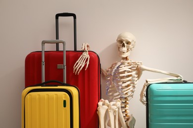 Waiting concept. Human skeleton with suitcases near light grey wall