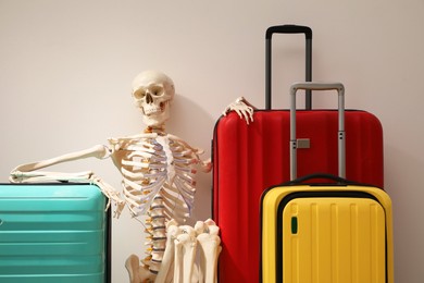 Waiting concept. Human skeleton with suitcases near light grey wall