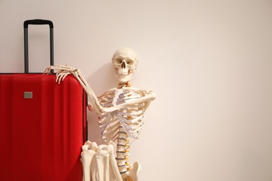 Waiting concept. Human skeleton with suitcase near light grey wall, space for text