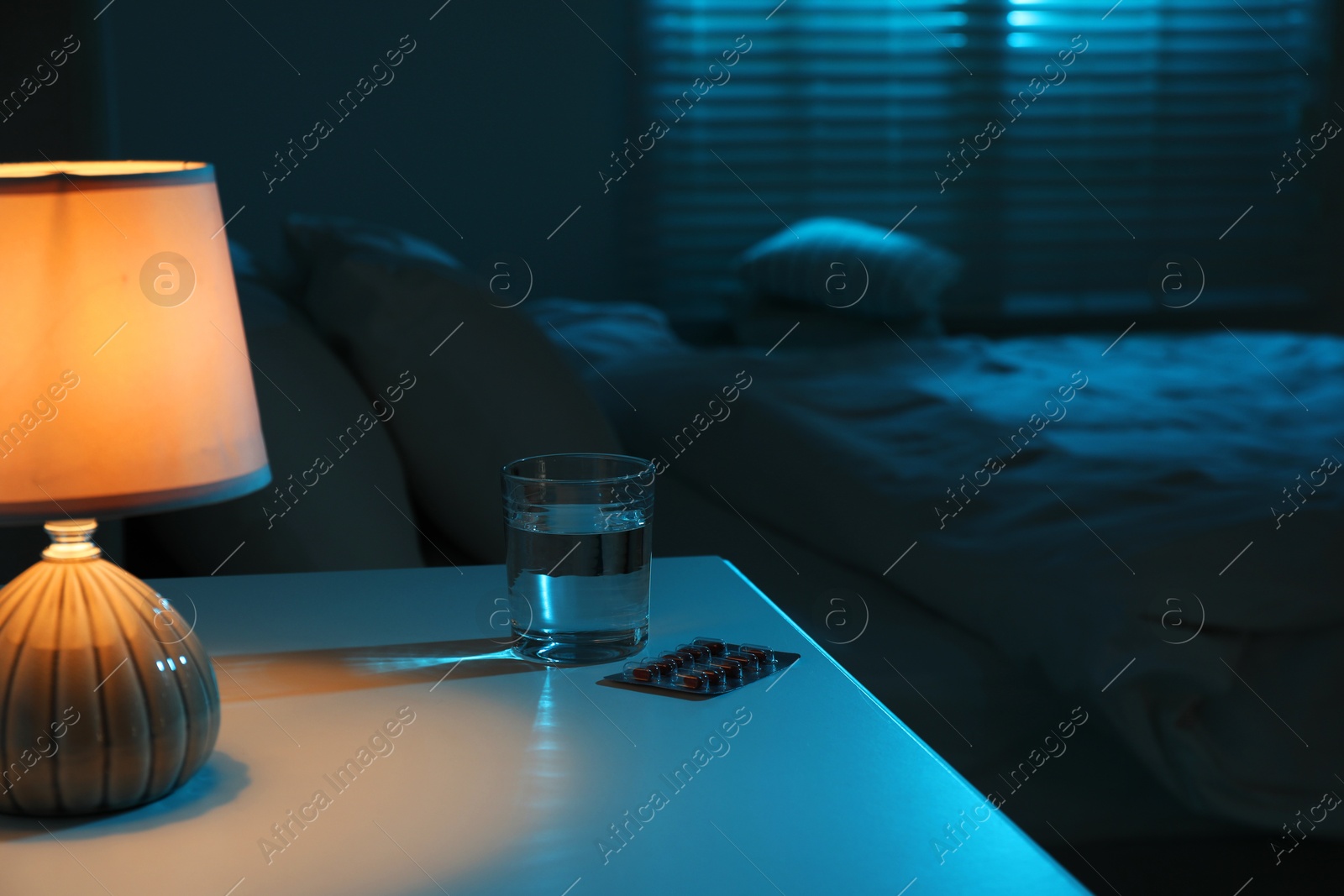 Photo of Insomnia treatment. Glass of water and pills on bedside table in bedroom at night