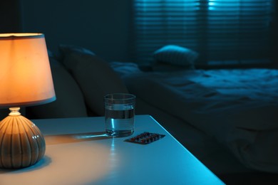 Photo of Insomnia treatment. Glass of water and pills on bedside table in bedroom at night