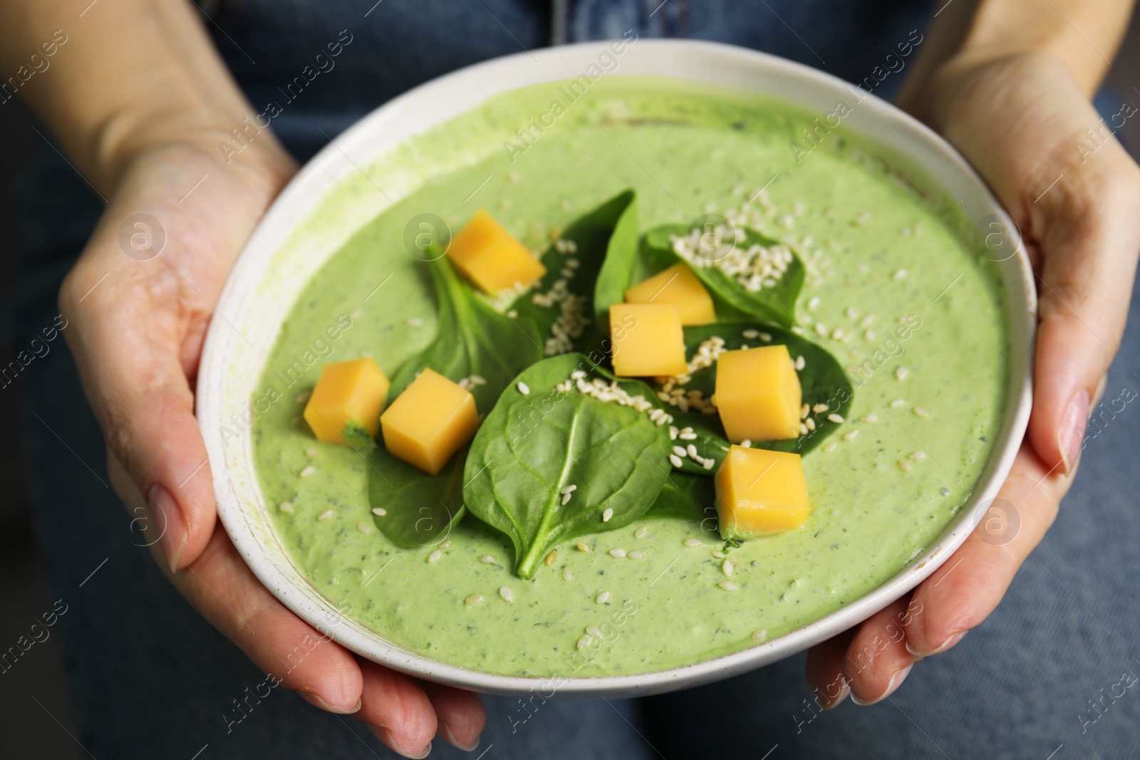 Photo of Woman holding bowl of delicious spinach cream soup, closeup