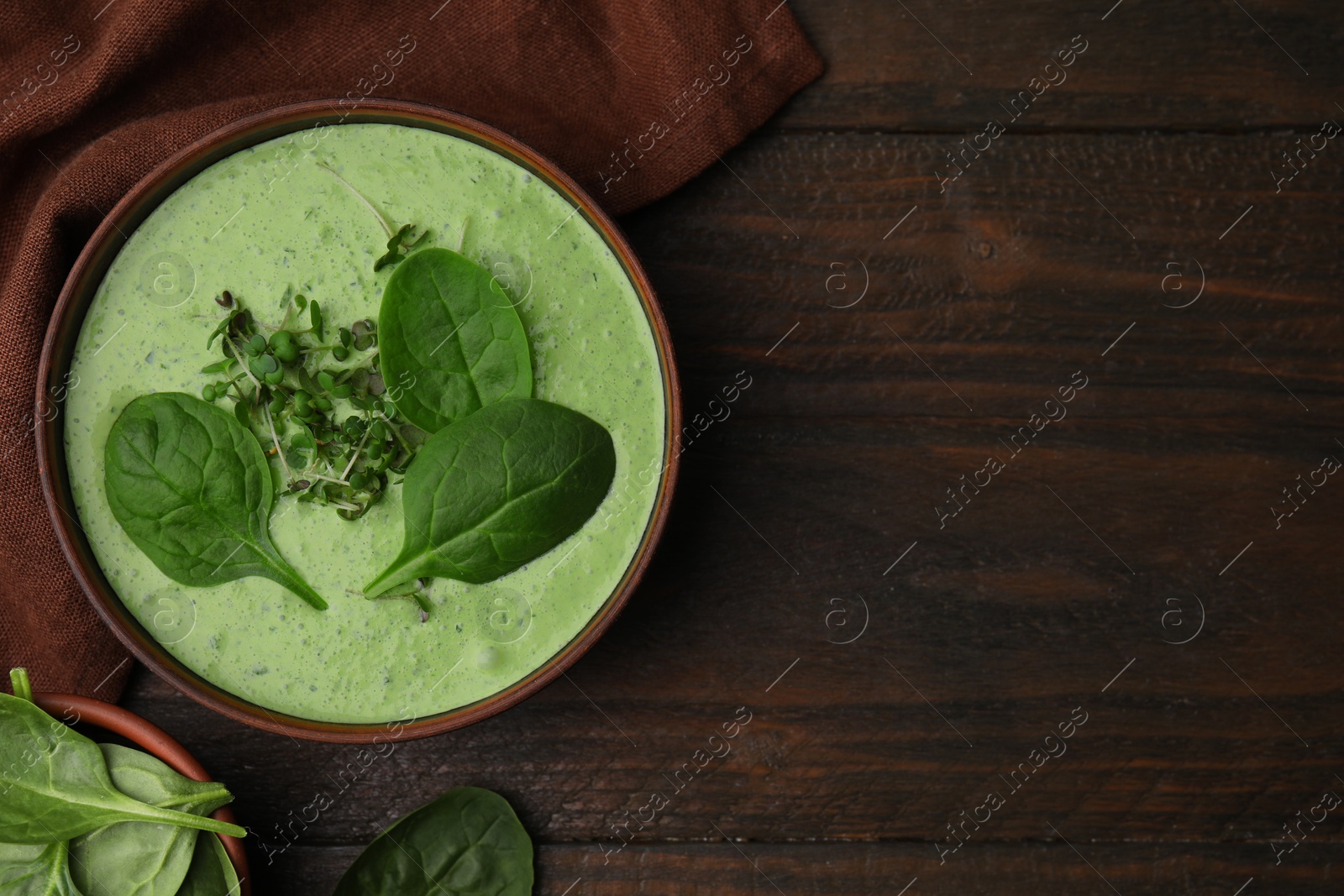 Photo of Delicious spinach cream soup with fresh leaves and microgreens in bowl on wooden table, flat lay. Space for text