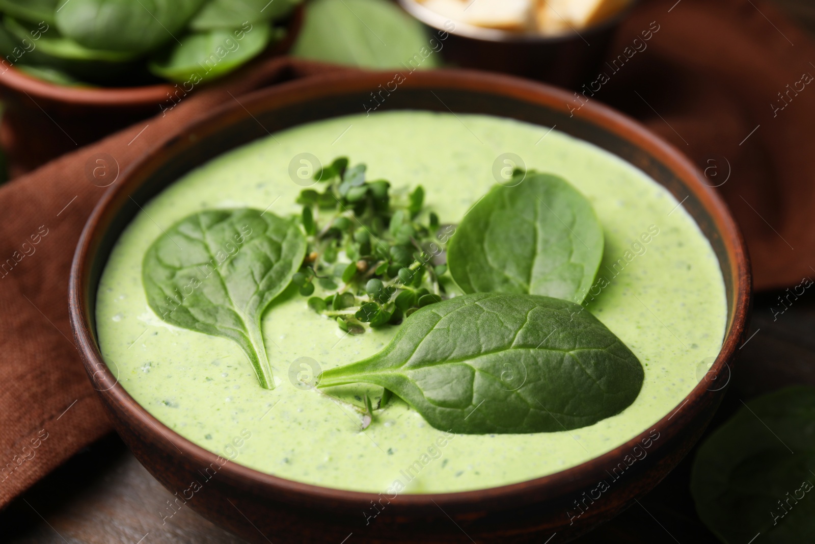 Photo of Delicious spinach cream soup with fresh leaves and microgreens in bowl on wooden table, closeup