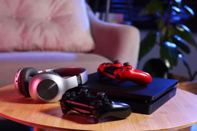 Video game console, wireless controller and headphones on wooden table indoors